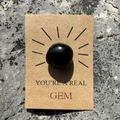 Polished black gemstone on a You're a Real Gem kraft card over natural stone - Obsidian