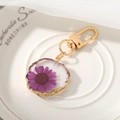 Detail of a purple dried flower resin keychain with gold serrated edges on white bone china - Purple Daisy