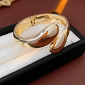 Dettaglio di un bracciale rigido dorato a forma di goccia su un porta gioielli - Oro