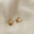 Detailed shot of gold hoop earrings with three zircon sliding rings on silk fabric - Gold