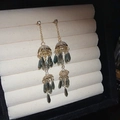 Detalle de pendientes largos dorados con borlas y cristales de gota gris oscuro en soporte - Dorado/Verde Grisáceo