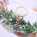 Primer plano de un llavero dorado con tres colgantes de flores en esmalte azul oscuro y detalles - Negro