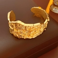 Macro shot of gold open bangle featuring irregular lava texture on dark leather base - Gold