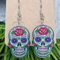 Nahaufnahme bunter Acryl-Ohrringe mit Totenkopf und Blumenmustern auf einer Karte - Bunter Blumen Sugar Skull