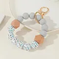 Detalle de cuentas de silicona y madera hexagonal en un llavero de pulsera con cierre dorado - Gris
