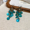 Pendientes bohemios flor de bronce con borlas de concha turquesa sobre fondo lino - Azul Lago