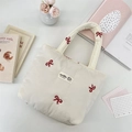 Detailed shot of a cream quilted canvas tote bag featuring delicate red bow embroidery - Red Bow