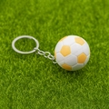 Macro d'un porte-clés mini ballon de football jaune et blanc sur fond d'herbe verte - Jaune