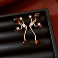 Dettaglio di orecchini dorati con pietre occhio di tigre e zirconi in scatola nera di lusso - Perno in Argento - Colore Oro - Stile Occhio di Tigre Caffè
