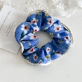Detail von blauem Blumen-Haargummi mit weißer Spitze und gelbem Blumendruck auf Holz - Blau Mit Spitzenkante