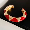 Dettaglio macro del bracciale aperto dorato con texture geometrica in smalto rosso - Stile Aperto Largo / Oro & Rosso