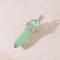 Light green hexagonal crystal pendant with silver metal clasp on a textured surface - Green Cat's Eye