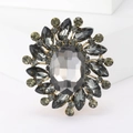 Elegante gouden broche met een groot grijs kristal en sprankelende smaragdgroene accenten - Zwart
