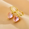 Close-up of heart-shaped pink zircon earrings with golden copper setting on peach fabric - Pink