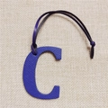 Close-up of blue lychee grain leather C-shaped bag charm with dark cord on linen - Letter C Royal Blue