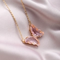 Detailansicht eines goldenen Schmetterlingsanhängers mit rosa Kristall auf Seide - Rosa