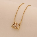 Close-up of a gold M-shaped pendant necklace with sparkling inlaid rhinestones - Letter M