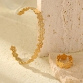 Close-up of matte 18K gold plated flower ring and open bangle on textured stone - Peach Blossom Style