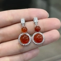 Close-up of hand holding silver earrings set with round red-orange chalcedony and zircons - Red Chalcedony Stud Earrings (White Gold Color)