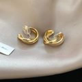 Detailed view of golden twisted metal ear clips on a premium beige silk fabric surface - Ear Clip - Gold