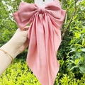 Pink large satin long tail bow hair clip held against a green outdoor background - Scarf Bow / Watermelon red