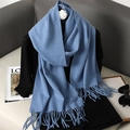 Blue solid cashmere-feel knitted scarf with fringe draped over a black top on a desk - Indigo Blue