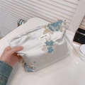 Gros plan d'une broderie florale élégante sur une trousse de maquillage en satin bleu - Bleu Élégant