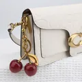 Close-up of white embossed leather bag with gold chain and red glitter cherry charm - Dark Red Apple with Bronze Gold