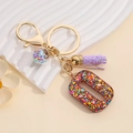 Macro detail of letter O keychain with purple tassel and colorful sequins in resin - Letter O