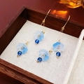 Detailed shot of long gold earrings with blue butterfly flowers on a wooden display - Blue Flower Style (Ear hook-Blue-Flower)
