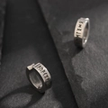 Macro detail of silver titanium steel ear clips with engraved black Norse runes on dark rock - Silver Rune