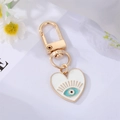 Detail of a golden heart keychain with a blue eye pattern on white background - White Heart Eyelash Eye