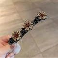 Elegant black hair clip with three gold and red rhinestone flowers held in hand - Champagne
