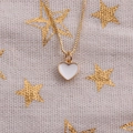 Close-up of golden box chain with white enamel heart pendant on starry fabric - White