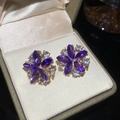 Gros plan de boucles d'oreilles fleurs mauves dorées dans un écrin en velours - Violet/Or (Tige en Argent)