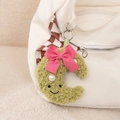 Detailed view of a green plush moon charm with a pink bow hanging on a checkered canvas bag - Sweet Moon Pendant