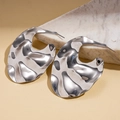 Close-up of irregular liquid-style silver metal earrings on minimalist stone props - Silver