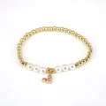 Macro detail of golden beaded bracelet with white pearls and pink zircon heart charm - Pink