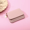 Pink leather wallet detail showing lychee texture and a gold round pendant tag - Pink