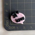 Close-up of pink resin LOVE charm with black bow on a measuring mat for sizing - Pink Base Black LOVE