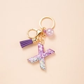Macro view of purple glitter resin letter X keychain with gold clasp and tassel detail - Letter X