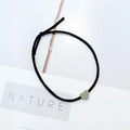 Detail eines schwarzen elastischen Haargummis mit kleinem grünem Herzanhänger im Natur-Stil - Graues Herz