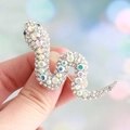 Silver snake brooch with green and champagne crystals held by hand against bokeh - White