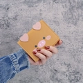 Portefeuille court en forme de cochon jaune tenu par un mannequin sur fond gris texturé - Jaune