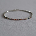 Detalle de pulsera tenis plateada con diamantes de colores sobre tela gris - 16cm / Plateado