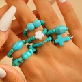 Cross and turquoise beaded ring set with white flower accents on hand display - 7-Piece Ethnic Turquoise Rings (3017) / Turquoise Blue
