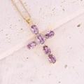 Dettaglio della collana a croce dorata con cristalli viola su superficie in pietra - Viola