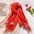 Detailed view of an orange-red cashmere-like scarf with tassels on a soft white vest - Orange