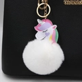 Llavero de unicornio de felpa con cadena dorada colgado en un bolso negro con textura - Blanco