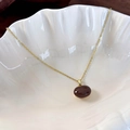 Macro shot of gold necklace with red bean pendant on a white shell tray - Brown